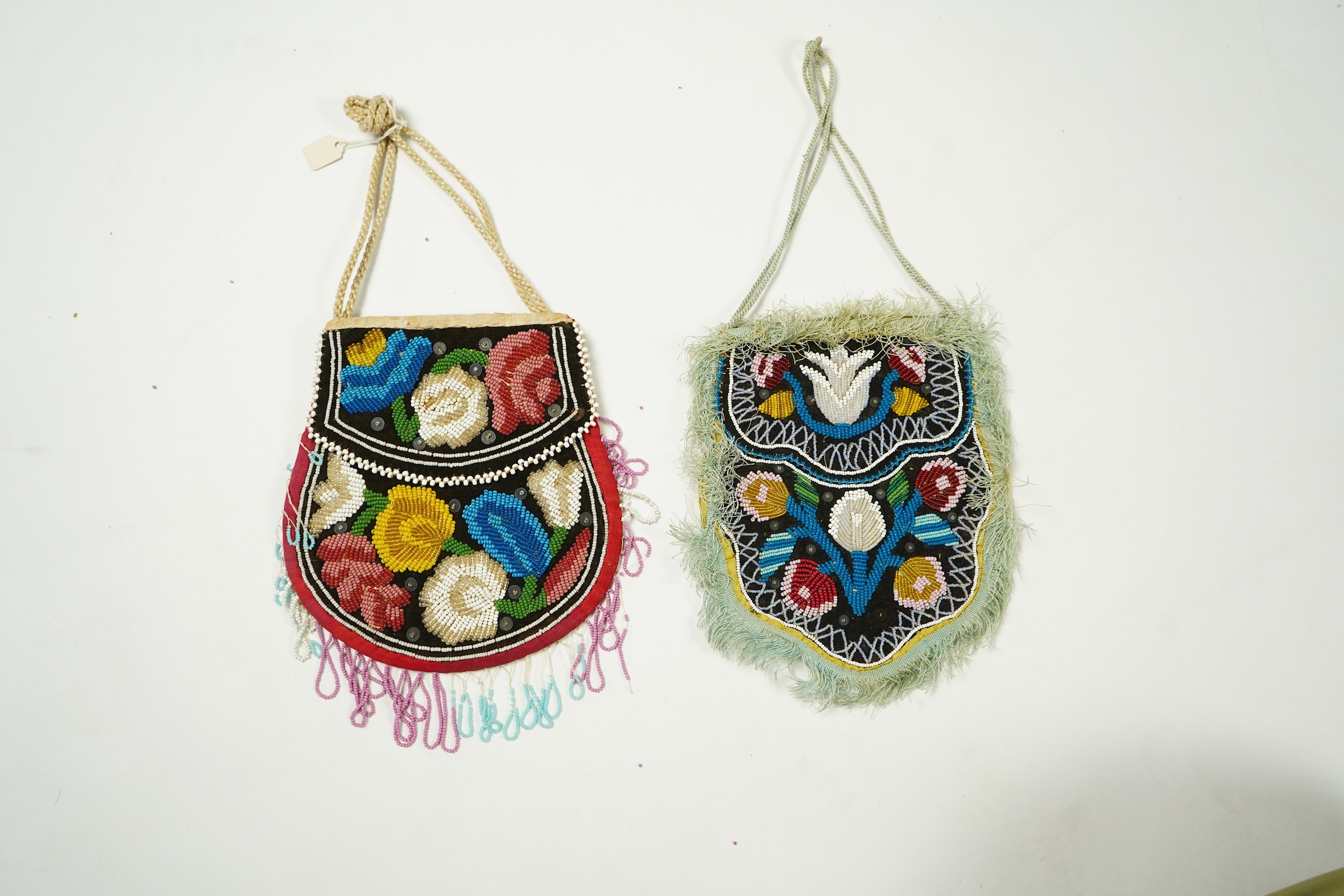 Two Native American Iroquois beaded bags. One edged with fine pale blue silk fringing, the other larger with bead worked fringing. Largest 16.5cm high. Condition - The blue fringed bag has a few sequins missing and the f